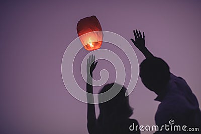 silhouettes of couple waving hands to flying chinese lantern in violet Stock Photo