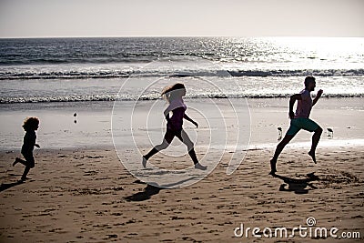 Silhouettes of family jogging along sea beach at sunrise. Outdoor workout, silhouettes of runners, sport and healthy Stock Photo