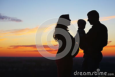 Silhouettes of father and son and a pregnant mom at sunset Stock Photo