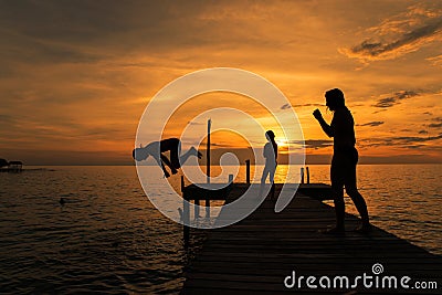 Silhouettes of kids jump into sea from pier Editorial Stock Photo