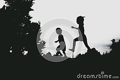 Silhouettes of kids jumping from a sand cliff at the beach Stock Photo