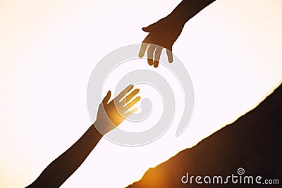 Silhouettes of man and woman helping each other to climb on hill against sunset Stock Photo