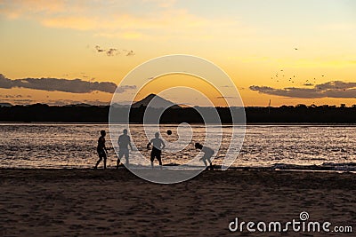 Silhouettes of People Playing Soccer on Beach at Sunset Time Stock Photo
