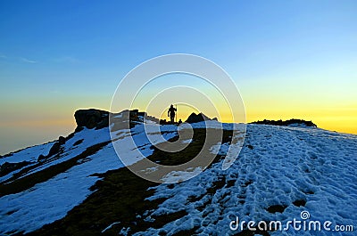 Silhouettes of People reaching at snow covered hill top after treacherous day long trek Stock Photo