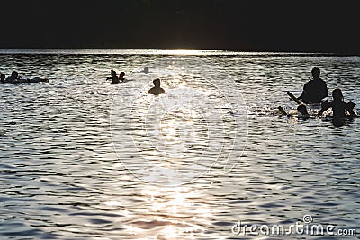 Silhouettes of people on a sunset lake background.Group of happy children having fun in summer lake or water Editorial Stock Photo