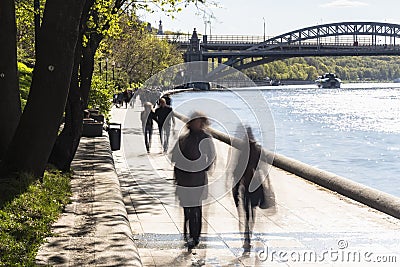 Silhouettes of people walk along the embankment of a city river Stock Photo