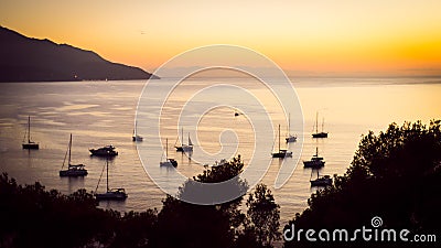 Silhouettes of private boats and small yachts anchored in a quiet bay in the Italian Mediterranean sea at sunset. Stock Photo