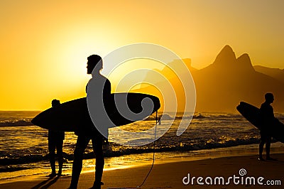 Silhouettes of surfers holding their surfboards on the background of golden sunset on Ipanema Beach , Rio de Janeiro Editorial Stock Photo