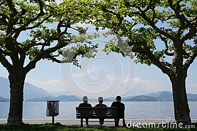 Silhouettes of three persons sitting on a bench. Editorial Stock Photo