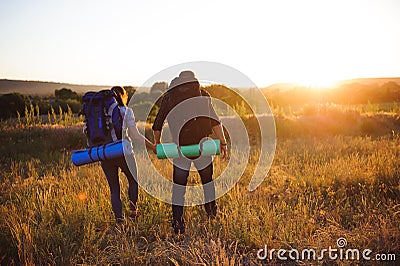 Silhouettes of two hikers with backpacks walking at sunset. Stock Photo