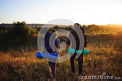 Silhouettes of two hikers with backpacks walking at sunset. Stock Photo