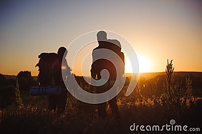 Silhouettes of two hikers with backpacks walking at sunset. Trekking and enjoying the sunset view. Stock Photo