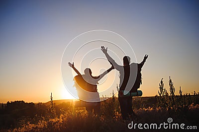 Silhouettes of two hikers with backpacks walking at sunset. Trekking and enjoying the sunset view. Stock Photo