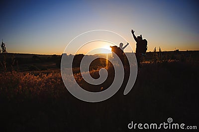 Silhouettes of two hikers with backpacks walking at sunset. Trekking and enjoying the sunset view. Stock Photo