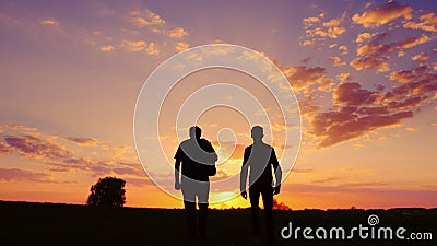 Silhouettes of two men - son and father go together to meet the sunset. Back view. Stock Photo