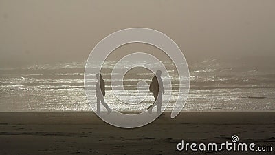 Silhouettes of two persons walking in an opposite directions on a Tillamook beach, Oregon Stock Photo