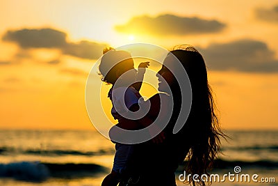 Silhouettes young mother with daughter playing and smiling on the beach at sunset. Happy family and travel concept. Stock Photo