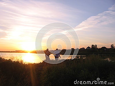 Silhouettes of a man and a girl on the lake in the rays of the setting sun Stock Photo