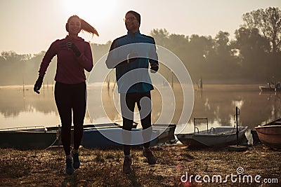 Silhouettes of young man and woman running by the lake or river in the early autumn morning Stock Photo