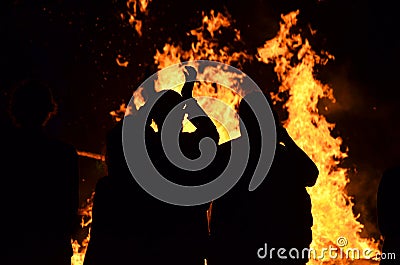 Silhouettes young people around roaring flames fire bonfire Stock Photo