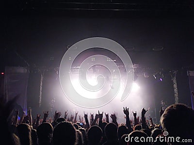 Silhouettes of young people with the raised hands up before a scene at a concert. Rock group. Bright light on the stage Stock Photo