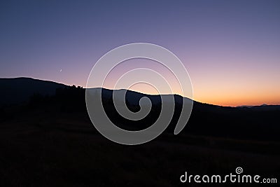 Silhoutte of evening mountains with trees on it and moon on the sky Stock Photo