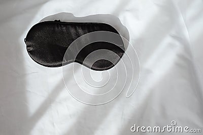 Silk black sleep mask without inscription on white rumpled sheets. Top view, flat lay. Horizontal. Copy spase. Concept of rest, Stock Photo