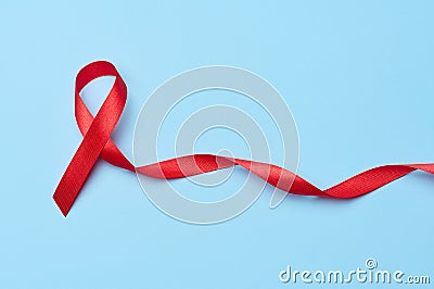 A silk red ribbon in the form of a bow is isolated on a blue background, a symbol of the fight against AIDS and a sign of Stock Photo