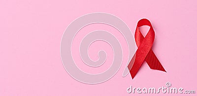 A silk red ribbon in the form of a bow on a pink background, a symbol of the fight against AIDS and a sign of solidarity and Stock Photo