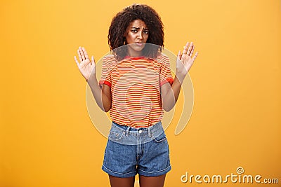 Silly insecure and sad dark-skinned female model in trendy striped t-shirt and shorts raising arms in surrender frowning Stock Photo