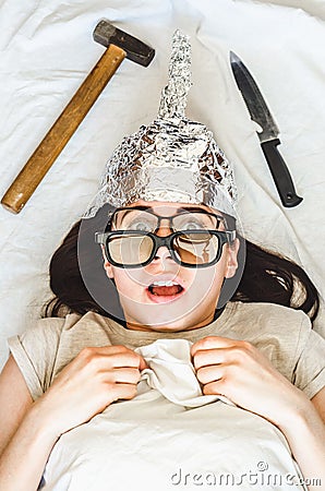 Silly paranoid woman wears tinfoil hat and sleeps with weapon and different glasses because of paranoia Stock Photo