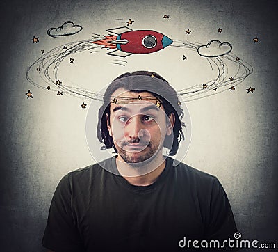 Silly young man makes funny dumb faces with crossed eyes. Body language emotional reaction. Dizzy daydreaming, stars and rocket Stock Photo