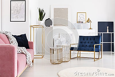 Silver painting on the wall of trendy living room with two elegant coffee tables, petrol blue armchair and powder pink Stock Photo