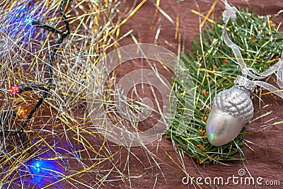 The silver acorn ceramic Christmas decoration on the branch of spruce with the colorful garland and tinsel. Stock Photo