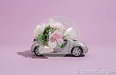 Silver convertible small car model with flowers on a purple background. The concept of delivery of flowers and gifts for the Stock Photo