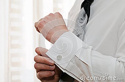 Silver cufflink that a man is putting on the cuff of his white shirt. Stock Photo