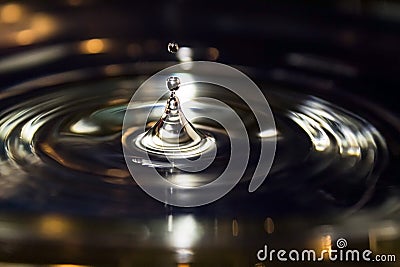 Silver drop jumping out of golden illuminated water Stock Photo