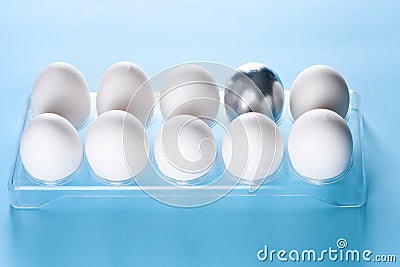 Silver egg in a plastic box with white eggs.Leadership, uniqueness, independence, new idea, initiative concept. Stock Photo