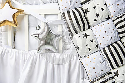 Silver and gold star shaped pillows and patchwork comforter on a white baby cot close up Stock Photo