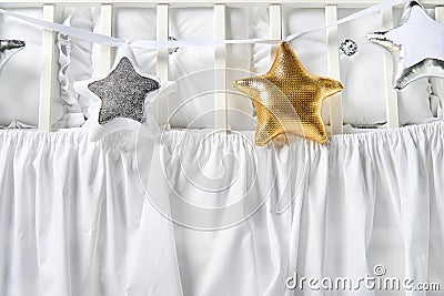 Silver, gold and white star shaped pillows on a white baby cot Stock Photo