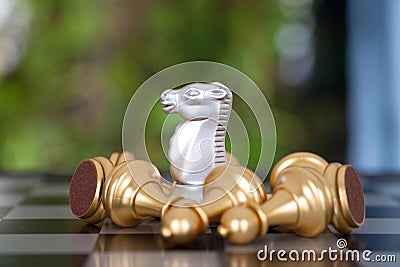 A silver horse piece surrounded by a pile of golden pawn pieces on a chess board Stock Photo