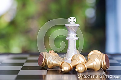 A silver king piece on a chess board surrounded by a pile of golden pawn pieces Stock Photo