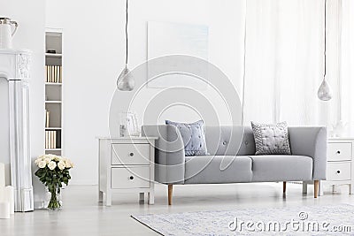 Silver lamps above white cabinets in apartment interior with flowers and grey settee. Real photo Stock Photo