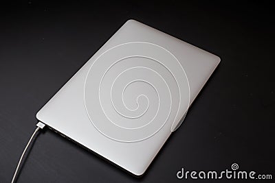 Silver laptop charging by magnetic connector on the black wooden background Stock Photo