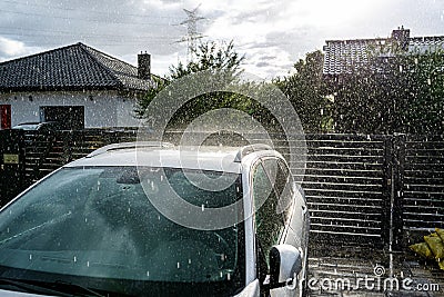 A silver passenger car parked in the driveway in front of the garage in the pouring rain during a downpour. Stock Photo