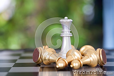 A silver queen chess piece surrounded by a pile of golden pawn pieces on a chess board Stock Photo