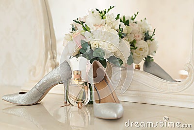 Silver shoes of the bride , perfume, bouquet and wedding rings on the dressing table near the mirror. Stock Photo
