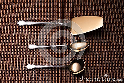 Silver shovel cake, teaspoon and spoon for sugar on the pattern table mat. Stock Photo