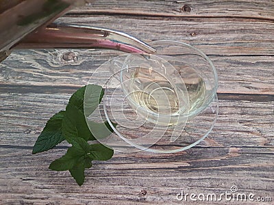 Silver teapot pouring peppermint tea (Mentha spicata) into a clear glass cup on a wooden table. Stock Photo