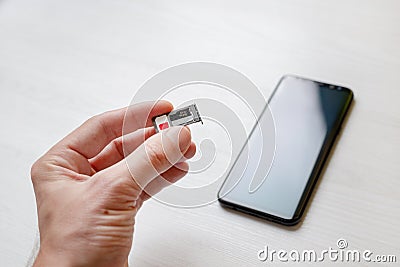 SIM card tray holder micro SD card slot adapter in hand. Smart phone in background Stock Photo